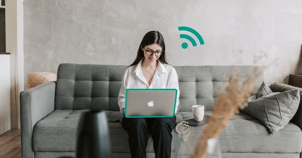 Fotografi på en kvinna som sitter i en soffa med en laptop i knäet. Hon har en illustrerad WiFi-symbol ovanför datorn som indikerar att hon har WiFi 6.